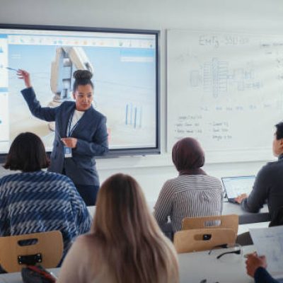University Robotics Lecture: Black Teacher Explain Engineering to Students. She Uses Interactive Whiteboard. Diverse Group of Young Engineers Listen in Class About Program Development for Robotic Arm.